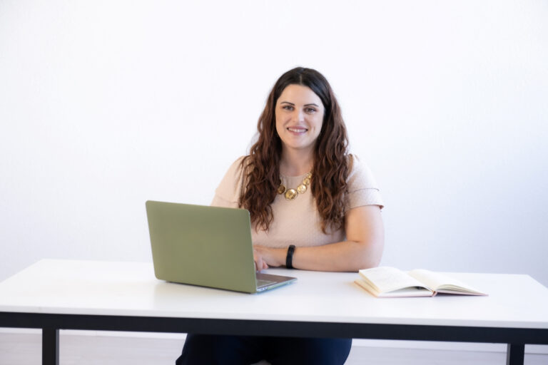 Woman sitting at a desk with a laptop and notebook, providing guidance on hiring a virtual assistant.