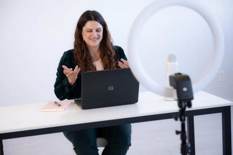 Smiling woman conducting a virtual meeting on her laptop, with a microphone and ring light on her desk, discussing time management.