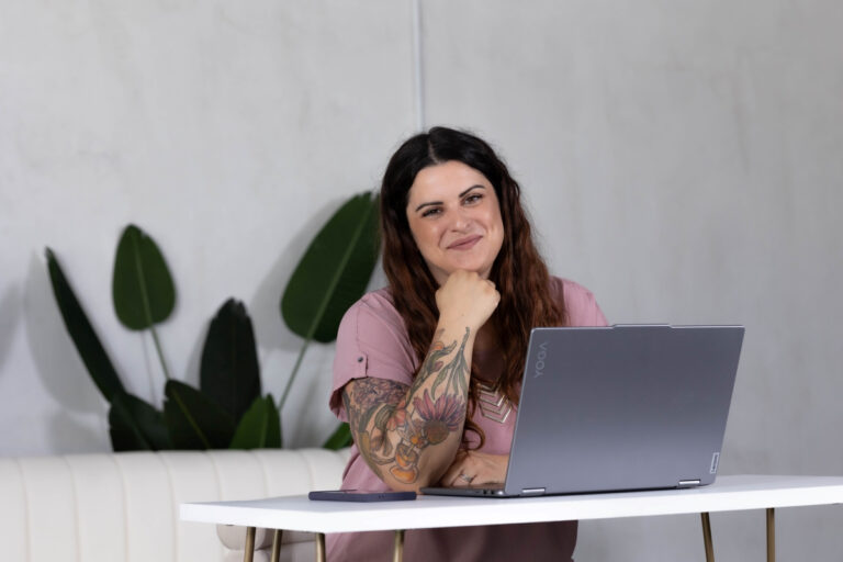 Smiling woman with tattooed arm sitting at a desk with a laptop, showing mindfulness and staying present throughout her workday.
