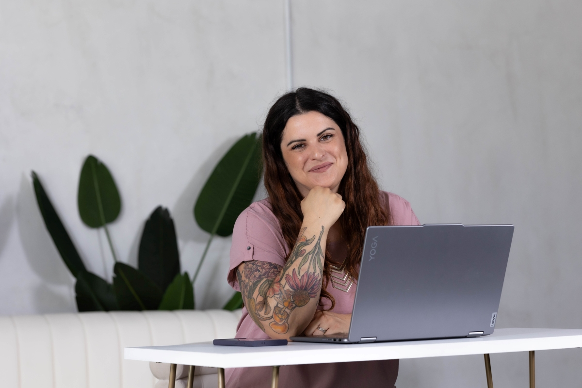 Smiling woman with tattooed arm sitting at a desk with a laptop, showing mindfulness and staying present throughout her workday.