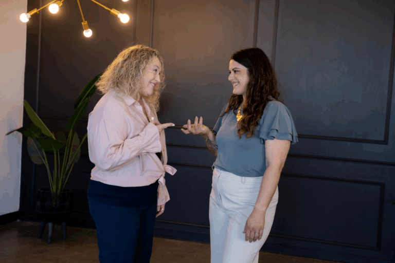 Two businesswomen engaging in a friendly conversation, representing collaborative business growth strategies.