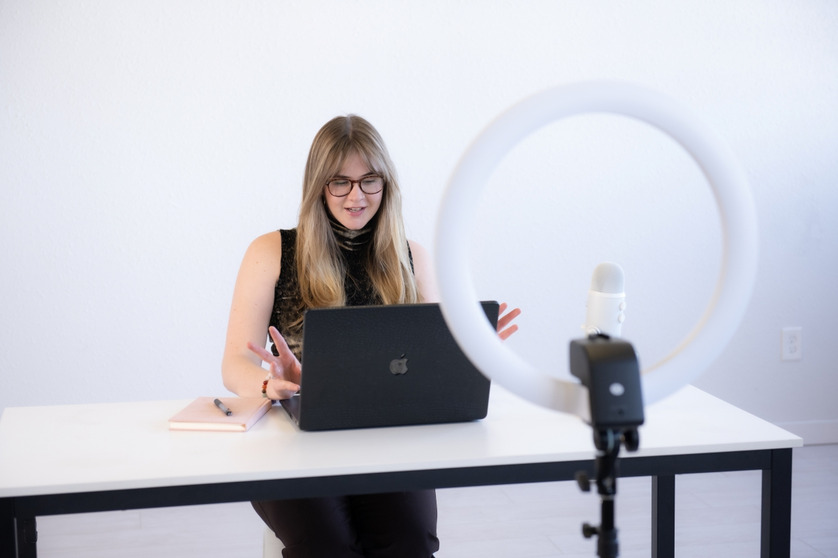 Woman hosting a virtual meeting with a laptop, ring light, and microphone — showcasing the benefits of hiring a virtual assistant for business efficiency.