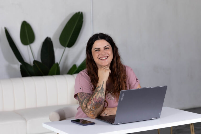 Smiling woman sitting at a desk with a laptop, representing a professional virtual assistant available for hire.