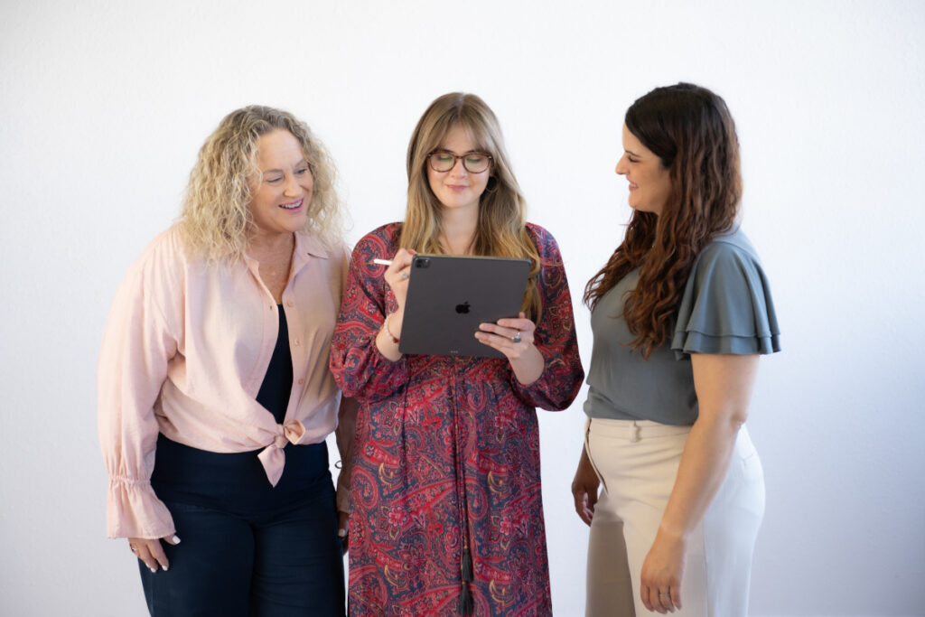 Three women reviewing a tablet together while collaborating on business operations and team processes.